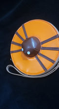 Load image into Gallery viewer, An orange wristlet wallet with a brown center resembling a spider laying on a donut, featuring a detachable strap.