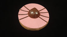 Load image into Gallery viewer, A light pink wristlet wallet with a brown center resembling a spider laying on top of a donut, featuring a detachable strap.