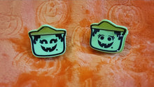 Load image into Gallery viewer, A set of two hair clips with designs resembling spooky buckets, with varying facial expressions, placed on an orange background with a Halloween theme.

