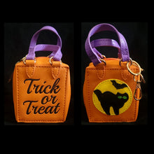 Load image into Gallery viewer, A double sided, mini Halloween trick or treat bag charm. A vibrant orange bag with purple handles, and gold hardware, has ‘Trick or Treat’ embroidered on one side and the other side features a moon with a spooky cat, and bat.

