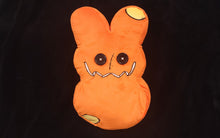 Load image into Gallery viewer, An orange plush backpack with a design resembling a Halloween Easter bunny with button eyes and a smile.
